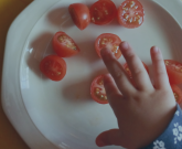 Child hand on top of a plate of tomatoes