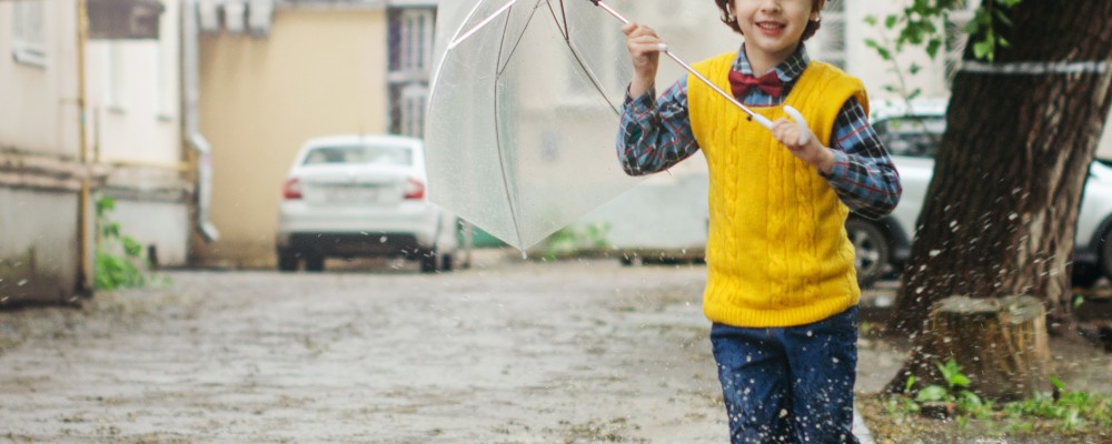 young boy running in rain with umbrella